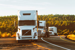 Multiple white cargo trucks driving on a road during mid day