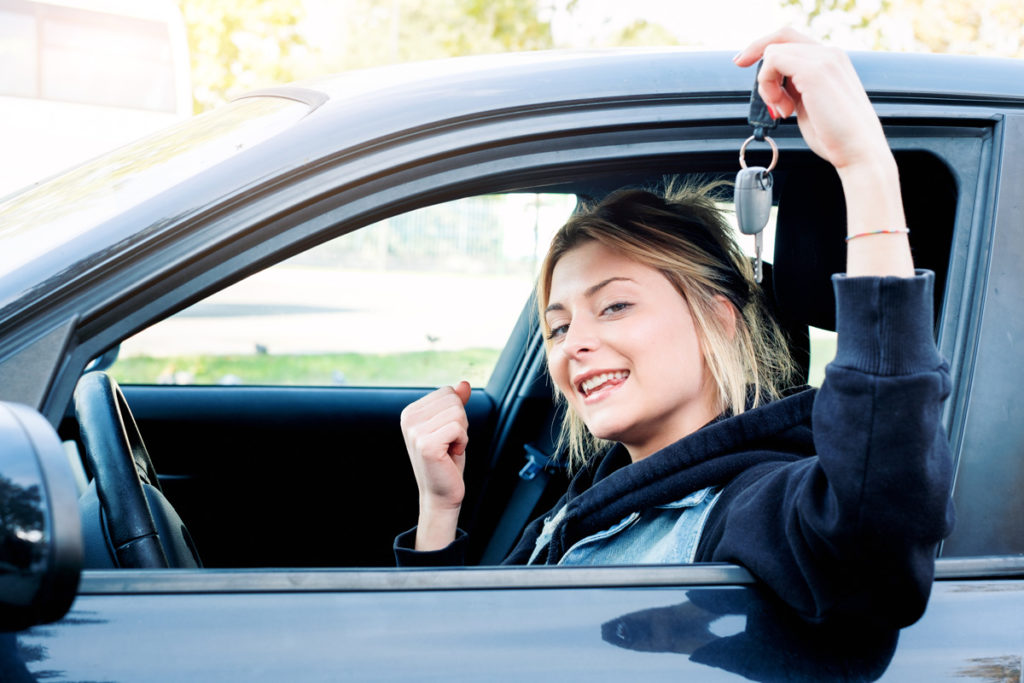 A young woman holding out a key from a car